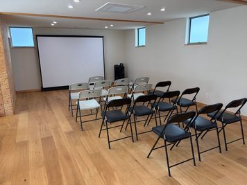【レイアウト例：セミナー】椅子を並べたシアター形式。大型スクリーン（100インチ）とスピーカーを使い、約18名規模のセミナーや上映会、発表会に最適です。 - スマイルベース粟津 スマイルカフェ2階 レンタルスペース＠粟津温泉の室内の写真