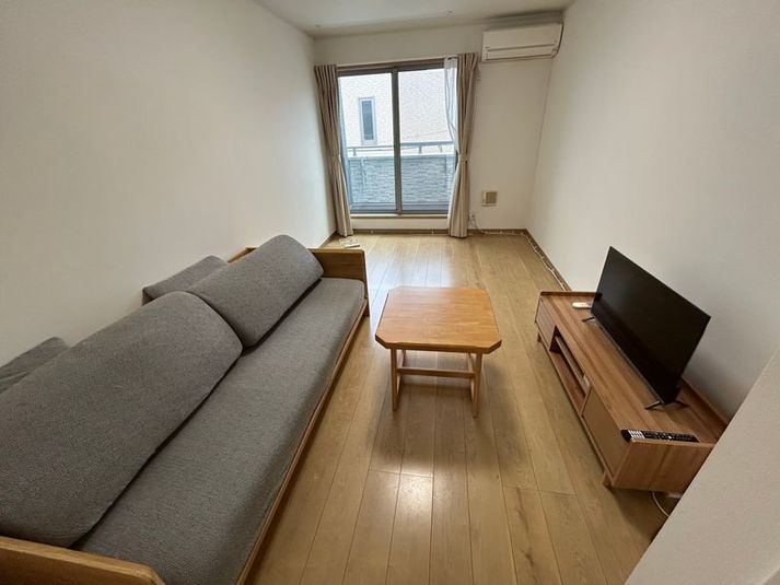 グレーの3人掛けソファと木製家具でまとめた、ナチュラルなお部屋。テレビで映画や動画鑑賞も楽しめます。 - Bed&City 北池袋 レンタルスペース 303号室｜3人掛けソファのあるナチュラルな完全個室の室内の写真