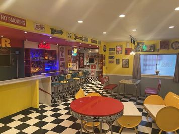 アメリカン雑貨が並ぶバーカウンターと、赤い丸テーブルやカラフルな椅子が特徴の店内。撮影からパーティーまで幅広く利用できる空間です。 - Darts＆Bar　MBY アメリカンダイナー貸切パーティースペースの室内の写真
