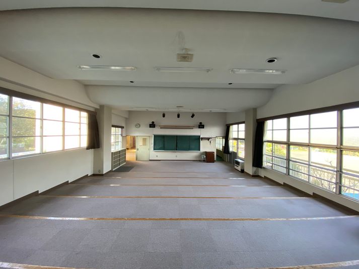 階段上の床と音楽室特有の天井の形状です。正面に黒板とスクリーンがあります。 - 八ヶ岳コモンズ シアターコモンズ（音楽教室）の室内の写真