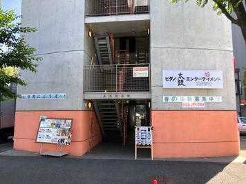 新幹線の線路沿いに、ベージュ色とコンクリートの不思議なツートンカラーのビルが目印です。 - ヒダノ太鼓エンタメスタジオ 完全防音の貸しスペースの入口の写真