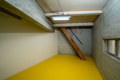 地下に降りる階段と剥き出し（コンクリート打ちっぱなし）＆黄色い床の地下室。 - 『ブルー・オーシャン戦略』の室内の写真