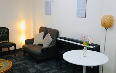 ２人掛けのソファ、電子ピアノ。暖色系の照明 - かちくらBASE まちのレンタル音楽室の室内の写真
