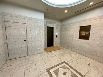 【1Fエレベーターホール_エレベーターまたは左の扉の先にある階段で2Fまでお上がりください】 - テレワークブース御徒町 天美ビル ブース08の入口の写真