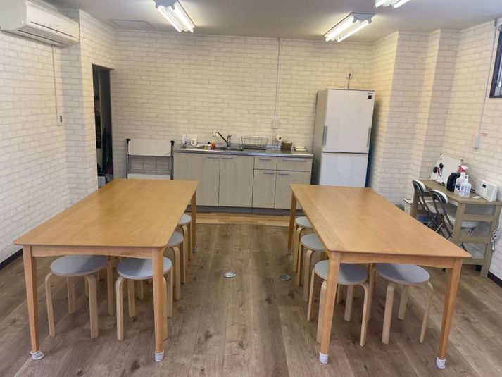 大きなテーブル、奥にキッチンと冷蔵庫、左手にトイレがあります - Hana Kitchen キッチン付きレンタルスペースの室内の写真
