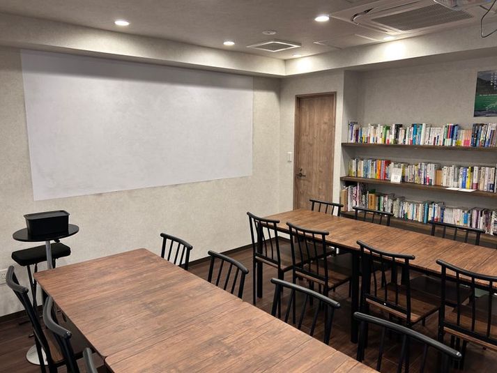 広々したテーブル席は、最大16人ご着席いただけます。本棚の本はご利用時間内にお手に取っていただけます。 - レンタルスペースQ プロジェクター完備 貸し会議室 上野・御徒町の室内の写真