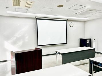 スクリーンの様子です。演台（写真左側）が1台、小さな台（プロジェクターを置く等活用いただけます）が1台あります。 - 世田谷産業プラザ会議室 貸し会議室（大会議室）の設備の写真